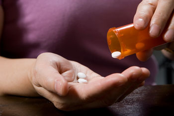 Person shaking prescription pills into their palm.