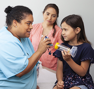 Health care provider showing child how to use metered-dose inhaler with spacer and mask.